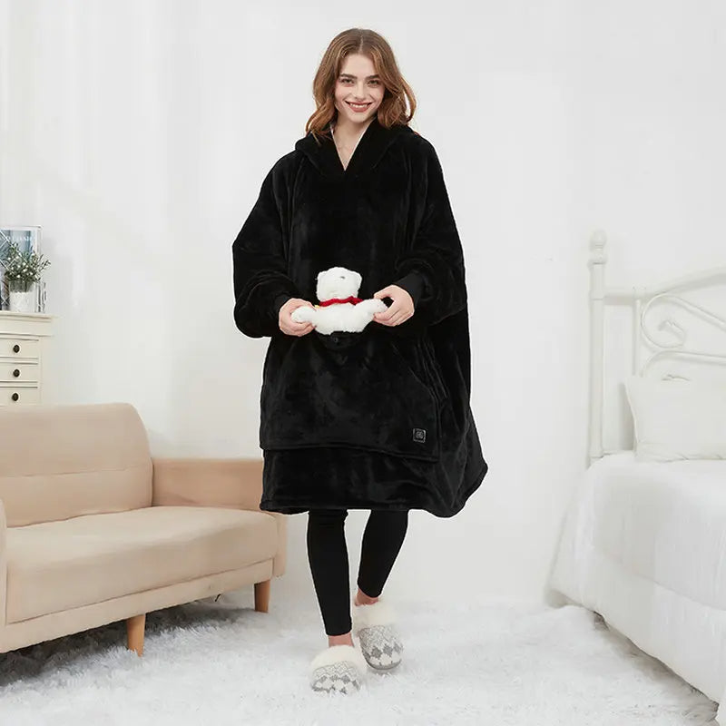 Woman wearing the oversized blanket hoodie in black, showing the full-length wearable blanket design with front pocket.