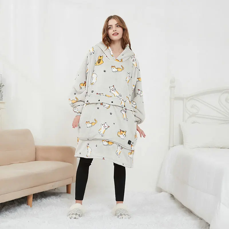 Woman wearing the oversized blanket hoodie in light grey cat, showing the full-length wearable blanket design with front pocket.