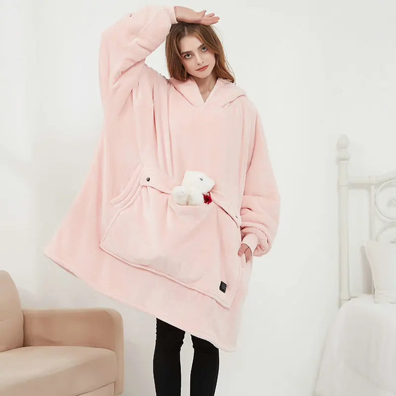 Woman wearing the oversized blanket hoodie in pink, showing the full-length wearable blanket design with front pocket.