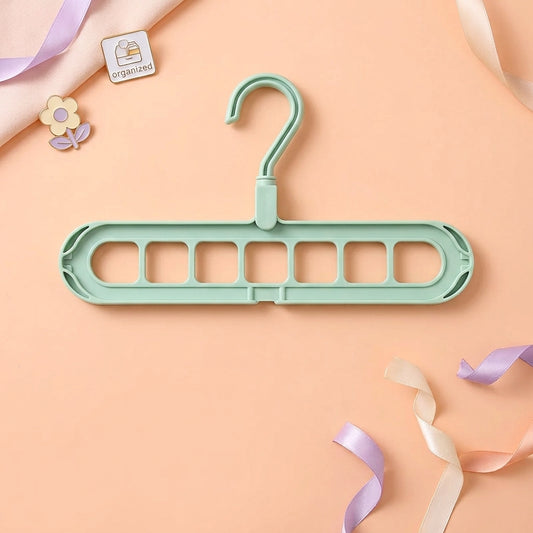 Green space saving coat hangers shown on a peach background, displaying the 9-hole cascading design that holds multiple garments in one slot.