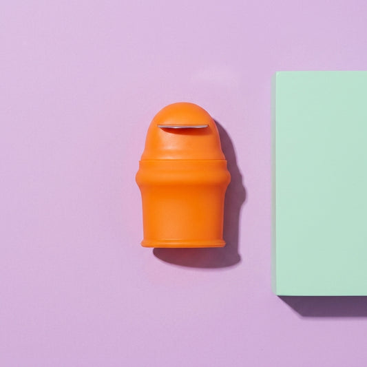 Orange silicone thumb knife shown on a purple background, featuring the stainless steel arc blade for garden harvesting.